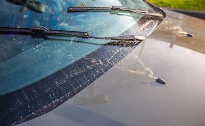 Windshield washer fluid is being sprayed from nozzles on the hood of a car onto the windshield.