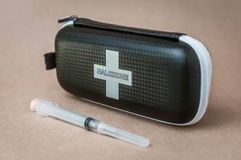 A black case with naloxone written on it behind a syringe connected to a needle