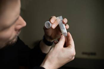 A person holding a small sample collection tube partly filled with saliva.