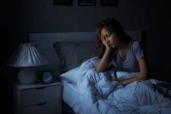 Woman sitting up in bed at night, holding her head in her hands