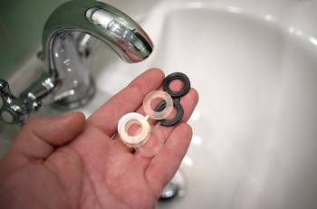 A hand holds black, white and colorless rubber plumbing seals in front of a faucet