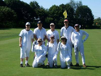Eight people in white cotton suits posing for a photo on a golf course green.