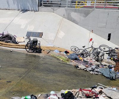 A concrete flood-control channel containing discarded items, including bicycles and a wheelchair.