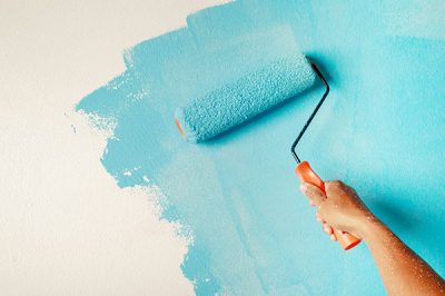 A person painting a wall with a paint roller.