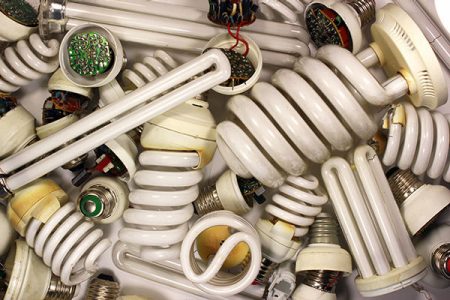 Several old spiral and tube-shaped fluorescent lamps that appear to be in a waste bin. 
