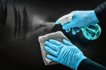 Gloved hands spray and wipe down a surface. 