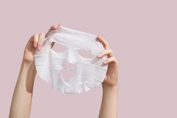 Hands holding up a white sheet mask with slots cut out in the middle for a person’s eyes, nose and mouth