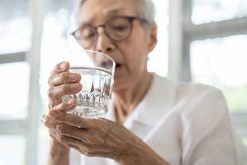 An older adult’s hands tremble while holding a glass of water. 